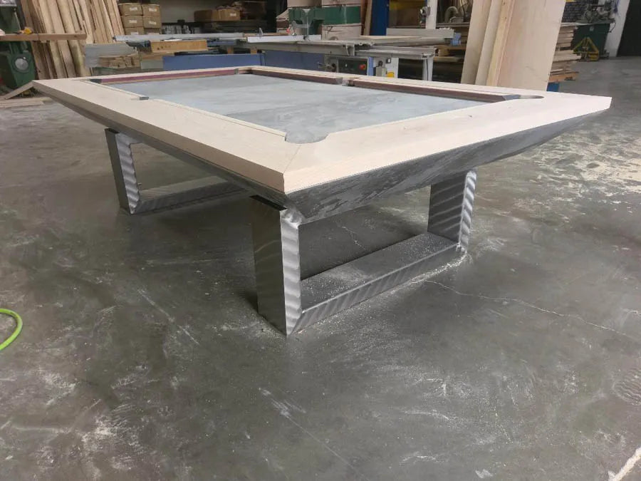 A custom pool table with a light wood top and metal legs in the workshop