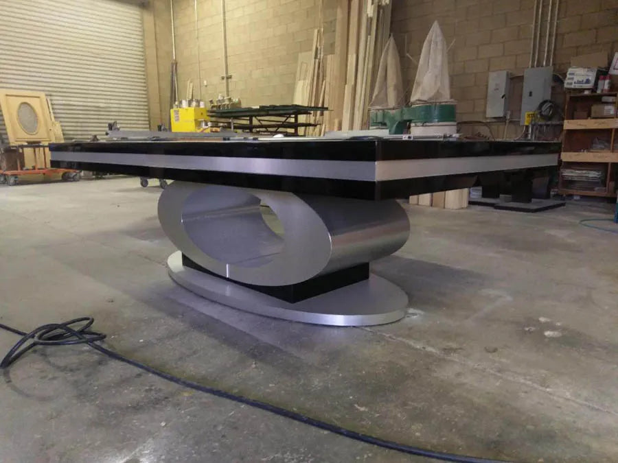 A custom pool table with a grey pedestal base and dark cloth in the workshop