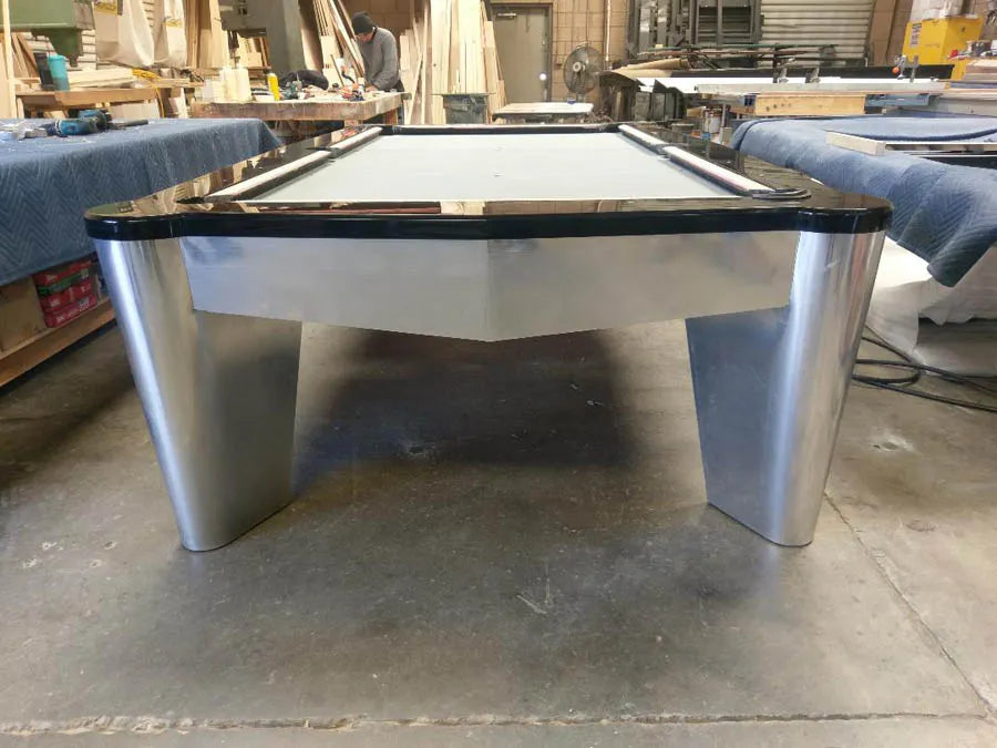 A custom pool table with tapered metal legs and dark cloth on the workshop floor