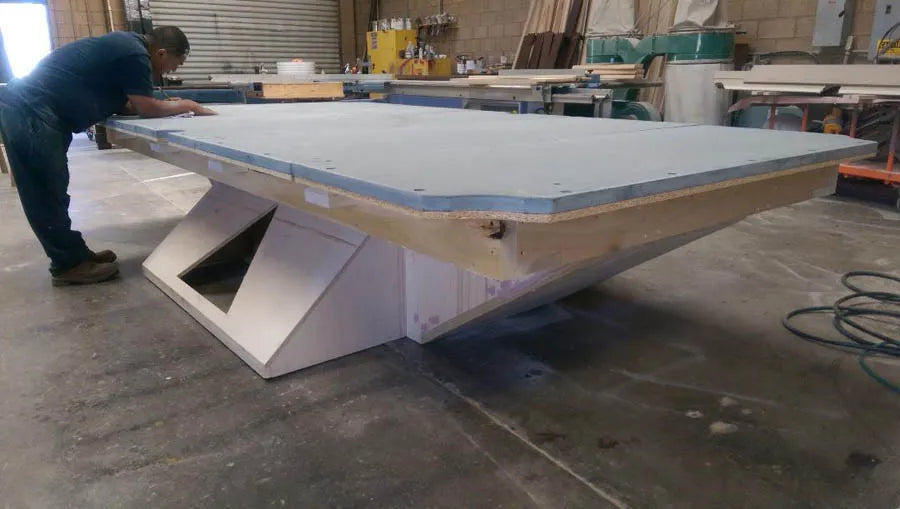 A craftsman building a custom pool table with a white angular base in the Norco workshop