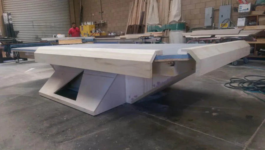 A custom pool table with a sculptural white angular base on the workshop floor