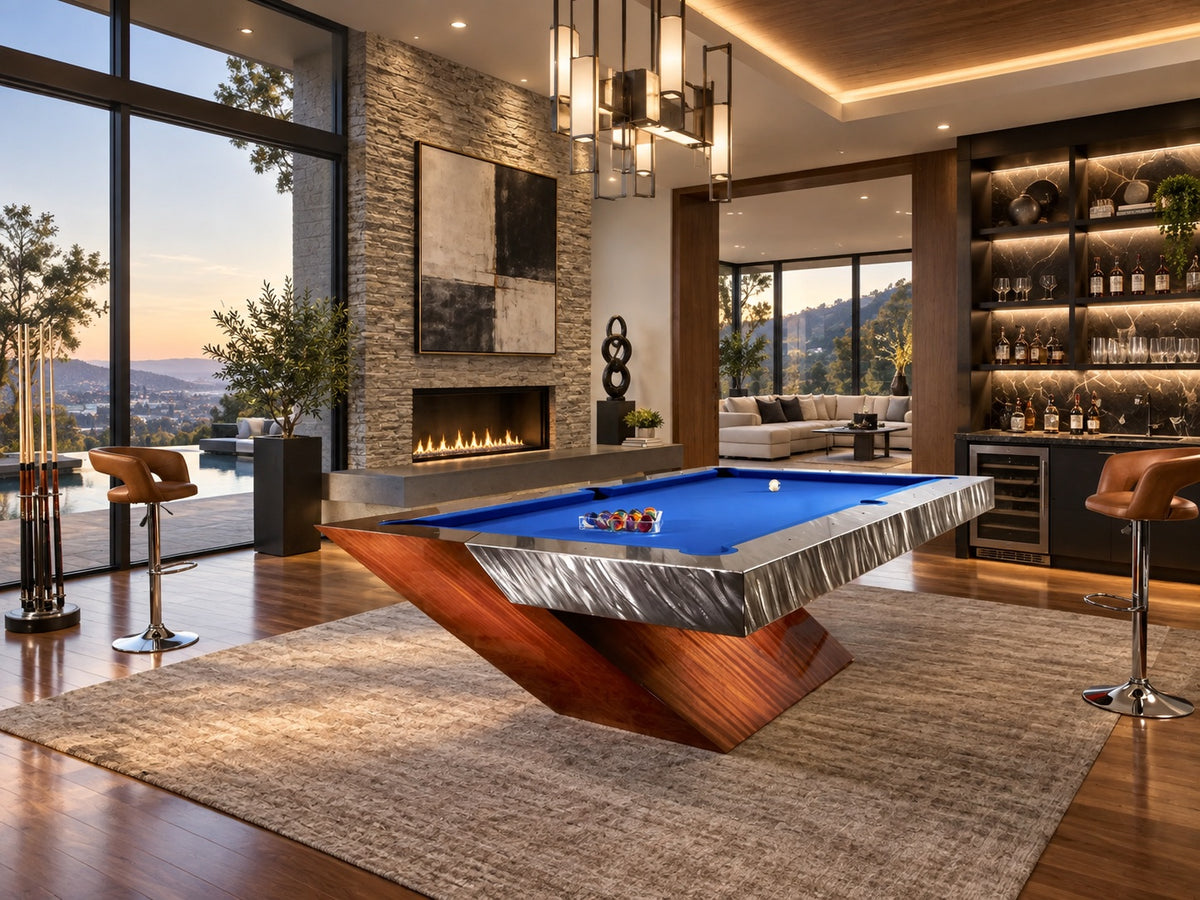 A pool table with royal blue cloth and a sculpted wood V-shaped base on a textured rug, in a game room with a stone fireplace